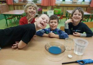 Dzieci siedzą przy stole z przygotowanymi materiałami do wykonania eksperymentu.